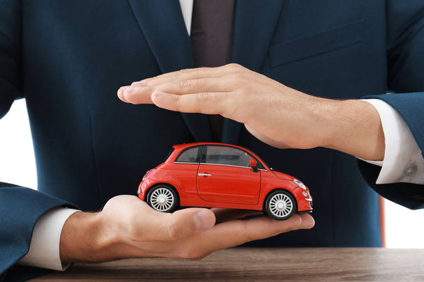 Pojišťovací agent drží autíčko nad stůl, zaměření na ruce - Fotografie, Obrázek