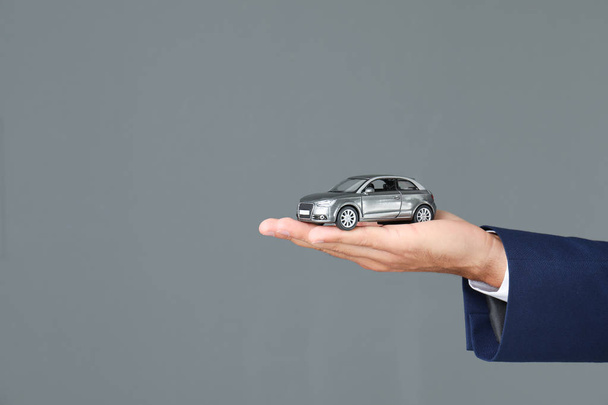 Versicherungsvertreter hält Spielzeugauto auf grauem Hintergrund, Nahaufnahme - Foto, Bild
