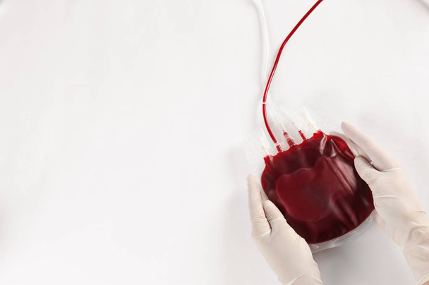 Doctor in gloves holding blood pack on white background, top view. Donation day - 写真・画像