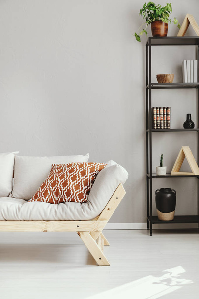 Patterned pillow on scandinavian sofa next to shelf with different kind of accessories, real photo with copy space - Valokuva, kuva