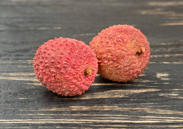 Two lychee fruit in shell closeup on a dark table - Photo, Image
