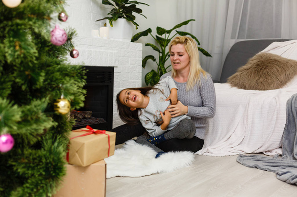 madre con hija hija hija sentada en el suelo cerca de la chimenea y el árbol de Navidad en el salón
  - Foto, imagen