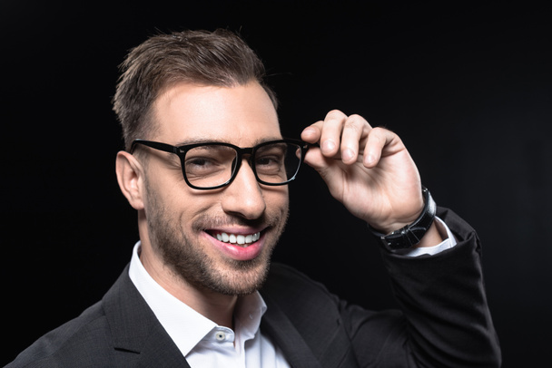 close-up portrait of handsome young businessman in eyeglasses looking at camera isolated on black - Fotó, kép