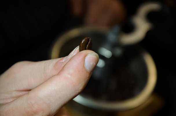 homme tenant un grain de café sur un fond flou d'un moulin à café
 - Photo, image