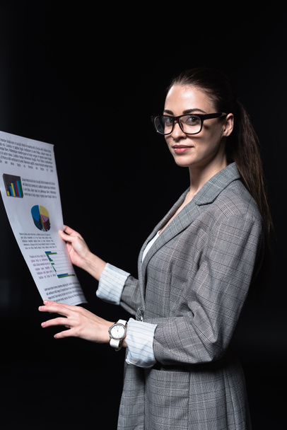 beautiful young businesswoman in stylish jacket holding newspaper isolated on black - Photo, Image
