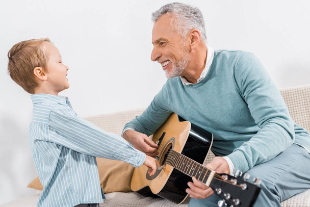 laughing middle aged man teaching grandson playing on acoustic guitar at home - 写真・画像