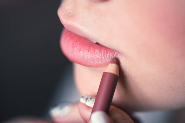 Woman putting on makeup, painting lips with red lipliner. Closeup of lips touched with pencil, studio. Small depth of field. - Zdjęcie, obraz