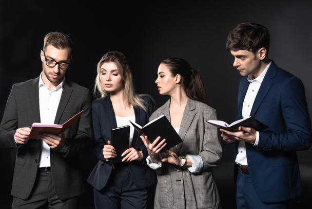 group of successful business people reading notebooks together isolated on black - Zdjęcie, obraz