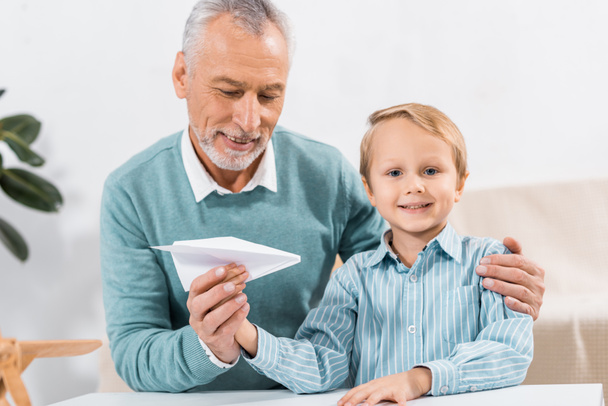 selective focus of grandfather and adorable grandson having fun with paper plane at home - Foto, afbeelding
