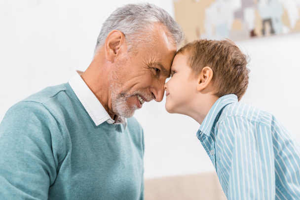 боковой вид счастливого мужчины средних лет лицом к лицу с маленьким внуком дома
 - Фото, изображение