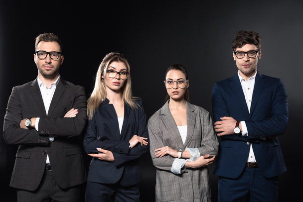 group of business people looking at camera together while standing in row with crossed arms isolated on black - Фото, зображення