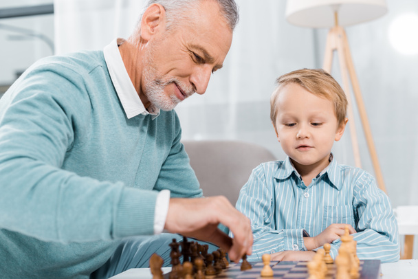selective focus of middle aged man teaching grandson to play chess at home - Фото, зображення