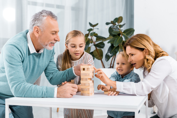 Happy παππούδες και τα εγγόνια να παίζει ξύλο μπλοκ πύργος παιχνίδι μαζί στο σπίτι - Φωτογραφία, εικόνα