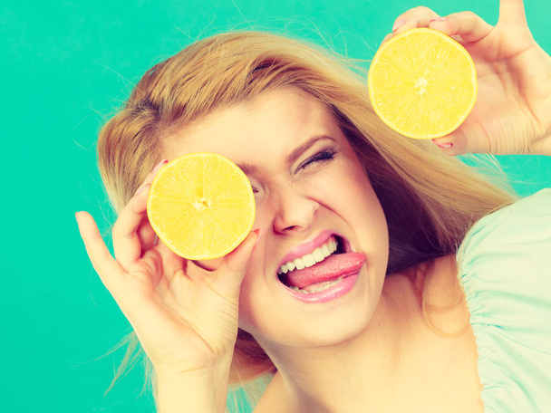 Woman teen girl holding two halfs of yellow lemon citrus fruit in hands, covering her eyes, on green. Healthy diet nutrition. Happiness fun concept. - Photo, Image
