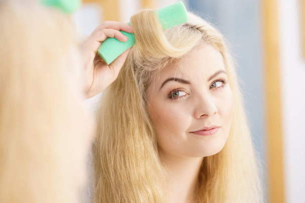 Blonde woman using hair rollers to create beautiful hairstyle on her hairdo. - Фото, зображення