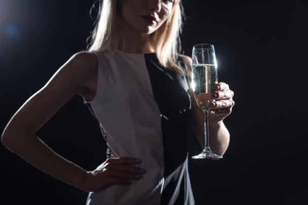 cropped shot of young woman holding glass of champagne on black - Fotó, kép