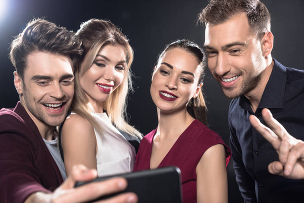 close-up shot of happy group of friends taking selfie with smartphone during party on black - Фото, зображення