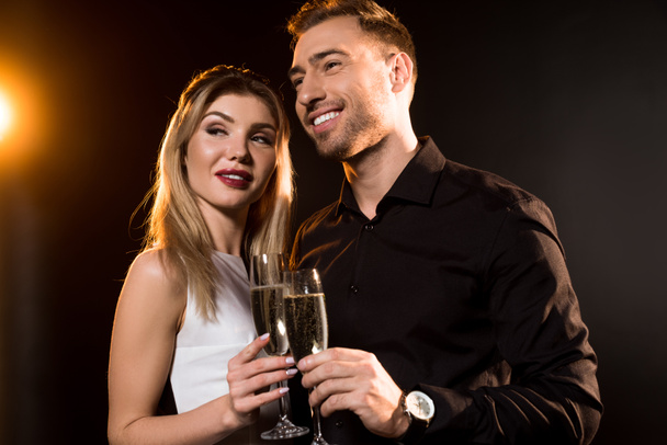 feliz joven pareja con copas de champán de pie juntos en negro
 - Foto, Imagen