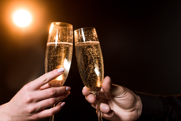 tiro cortado de copos de clinking par de champanhe sob luz dourada em preto
 - Foto, Imagem