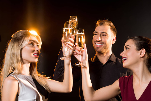 grupo de amigos sonrientes tintineo copas de champán bajo la luz dorada en negro
 - Foto, Imagen