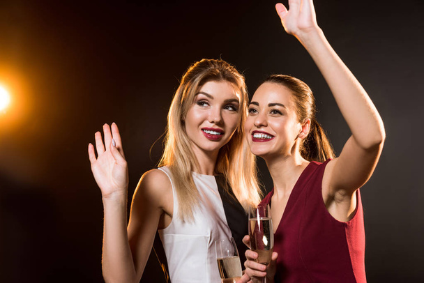 beautiful young women in dresses with champagne glasses waving on black during new year party - Foto, Bild
