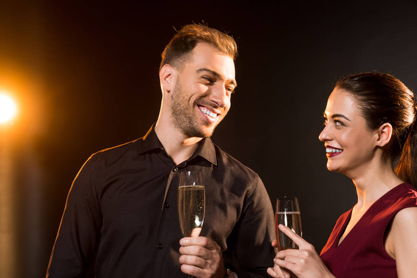 happy young couple with glasses of champagne flirting on black - Φωτογραφία, εικόνα