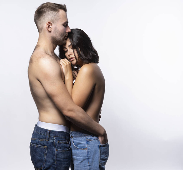 A beautiful couple wearing jeans and stripped to the waist stand sideways. A man hugs a girl. Casual style. Lifestyle, fashion, love, commercial design. Isolated on white. Copy space. - Fotoğraf, Görsel