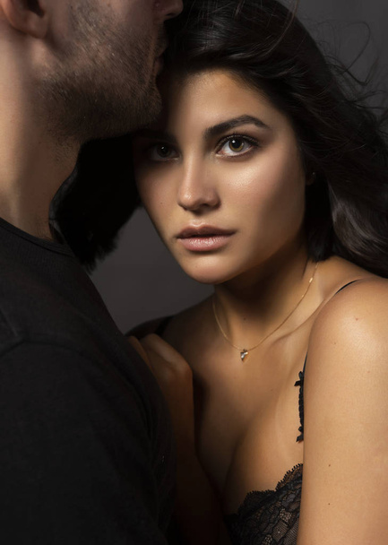 Closeup of a beautiful couple. A man sensually touches his lips to the forehead of a girl whose shoulder is bare. Casual fashionable style. Lifestyle, fashion, commercial design. Gray background. - Photo, image
