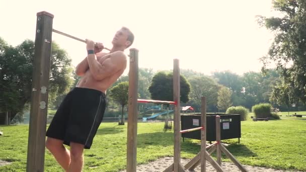 young man doing bodyweight exercises at horizontal bar on stadium - Materiał filmowy, wideo