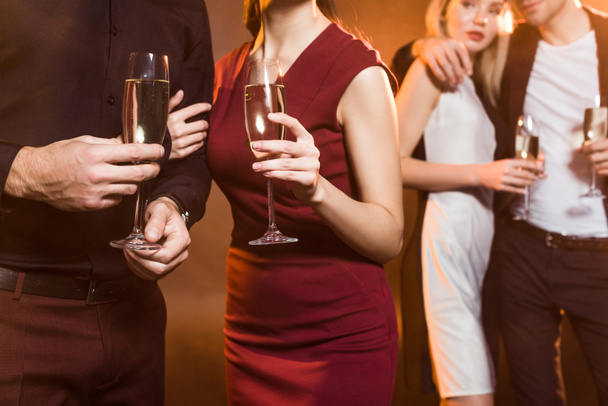 tiro recortado de parejas con copas de champán de pie bajo la luz dorada durante la fiesta
 - Foto, imagen
