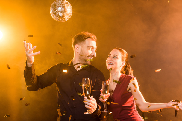 feliz pareja coqueteando con champán divertirse durante la fiesta bajo la luz dorada mientras confeti cayendo alrededor
 - Foto, Imagen