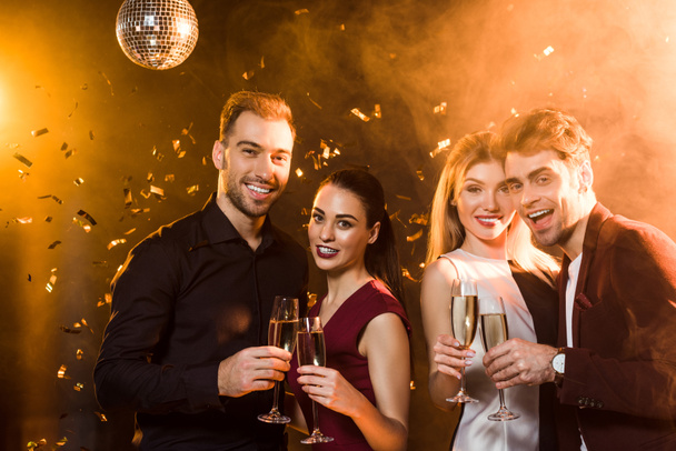 happy group of friends holding glasses of champagne and looking at camera during party - 写真・画像