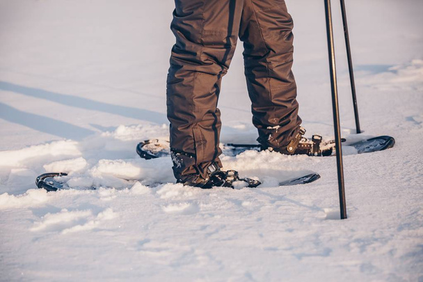 Man with snowshoe on the snow path close-up. Man in snowshoes with trekking poles in winter Finland - Photo, image