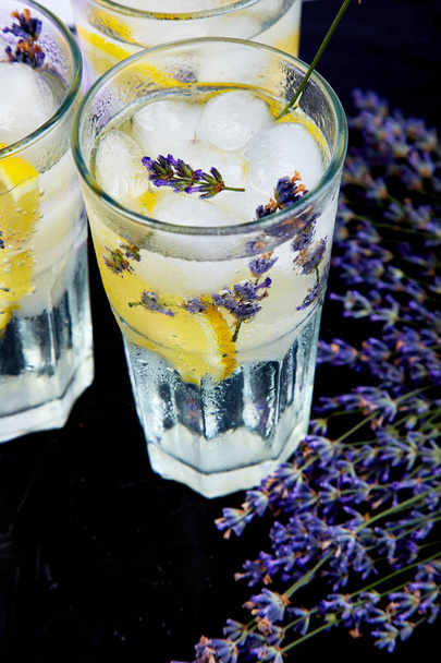 Lavender lemonade with lemon and ice on black background. Detox water. Summer drink. Diet cocktail. Beautiful. - Photo, Image