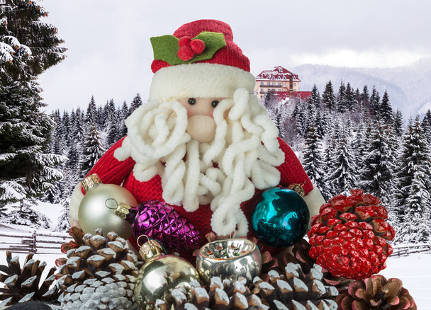 Oyuncak Noel Baba Noel süsleri arka planda dağlar karla kaplı ormanda ile bir kış manzarası ve bir tepe üzerinde kırmızı çatılı evler ile. - Fotoğraf, Görsel