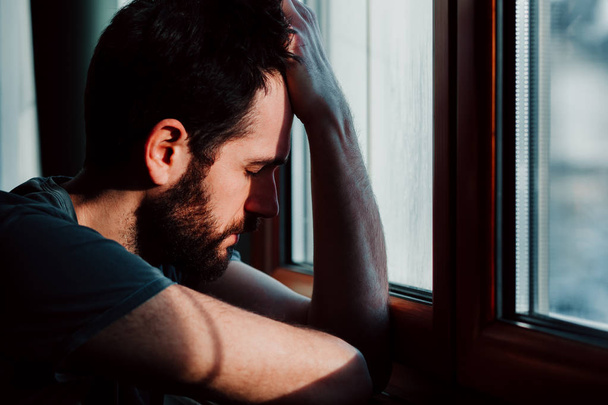 Vousatý mladý muž u okna v zoufalství  - Fotografie, Obrázek