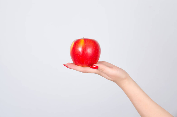 Red apple in the palm of the hand of a young woman on a gray background close-up - Valokuva, kuva