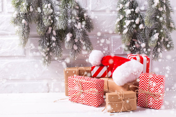 Winter vakantie decoraties. Verpakte kerstcadeautjes, decoratieve kerstmuts, bont boomtakken op wit gestructureerde achtergrond. Selectieve aandacht. Getekende sneeuw. - Foto, afbeelding