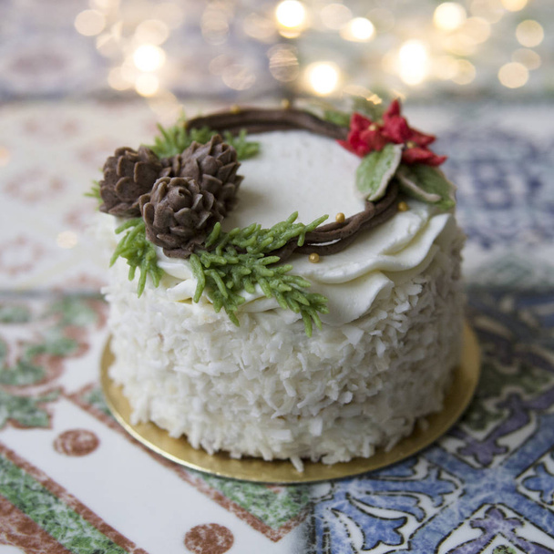 White New Year or Christmas cake decorated with cream poinsettia flowers, pine cones, cotton and spruce twigs on a colorful table. A birthday cake for those born in winter. Copy space, selective focus - Fotó, kép