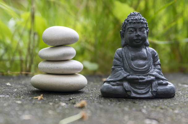 Harmony and balance, simple pebbles tower in the grass, simplicity, four stones and dark grey Buddha statuette - Foto, Bild