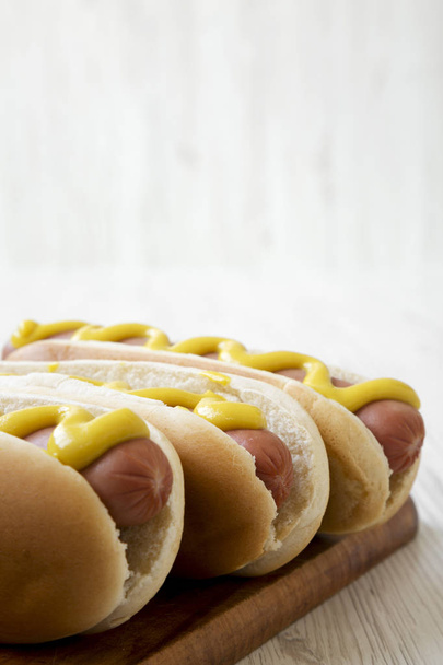 Hotdog с желтой горчицей на деревянной доске на белом деревянном фоне, вид сбоку. Копирование пространства
. - Фото, изображение