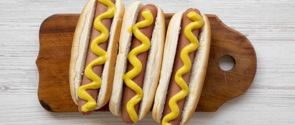 Domácí hot-dogy žluté hořčice na rustikální dřevěné desce na bílém pozadí dřevěná, pohled. Pohled shora, ploché ležel, shora. Detail. - Fotografie, Obrázek