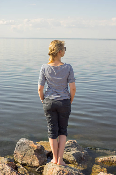 Красива молода дівчина в сірому смугастому светрі з білим волоссям стоїть на каменях на тлі озера
. - Фото, зображення