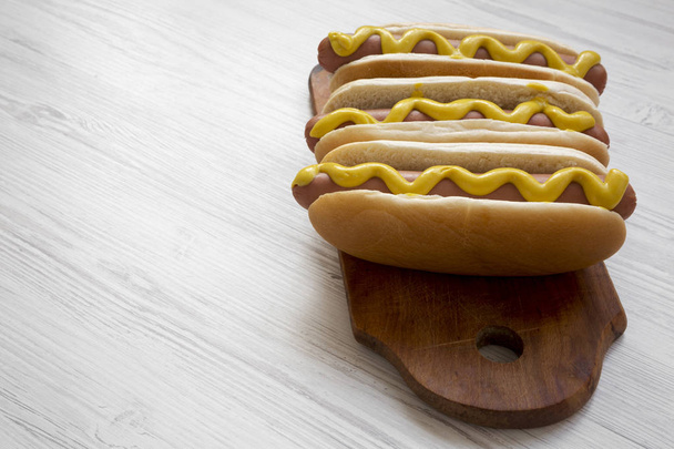 Hot dog con senape gialla su tavola di legno su sfondo bianco in legno, vista laterale. Copia spazio
. - Foto, immagini