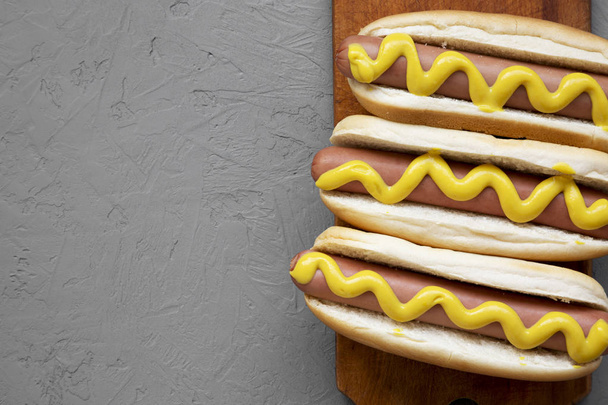 hausgemachte Hot Dogs mit gelbem Senf auf Holzbrett über Betongrund, Draufsicht. flach, über Kopf, von oben. Kopierraum. - Foto, Bild
