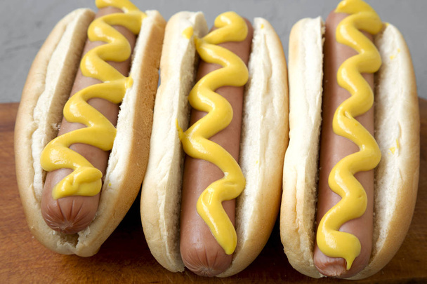 Tasty hot dogs with yellow mustard on wooden board on grey background, side view. Close-up. - Foto, Imagen