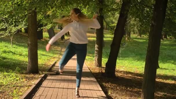 Mujer rubia bastante caucásica está practicando la danza latina y dando pasos desde la cámara hacia el hermoso parque verde de verano, moviéndose en la pista
 - Metraje, vídeo