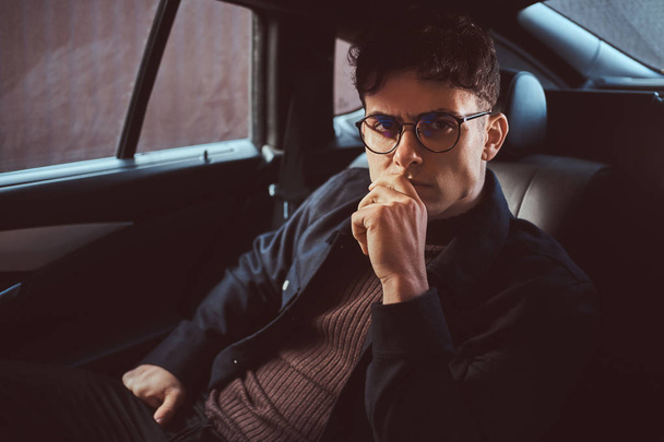 Un jeune homme cher portant des lunettes assis sur le siège arrière de la voiture
. - Photo, image