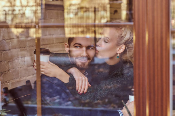 Beautiful girl sitting on her boyfriends lap on the cafe behind the window. - Photo, Image