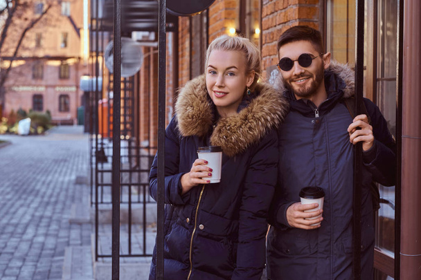 テイクアウトのコーヒーを保持している冬のコートを着て魅力的なカップルを笑顔 - 写真・画像